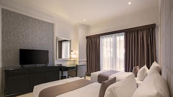 A hotel room with two beds, a desk, a television, and a large window with curtains.