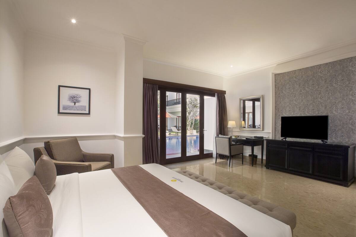 Une chambre d’hôtel équipée d’un lit, d’un bureau, d’une chaise, d’une télévision et offrant une vue sur une piscine extérieure.