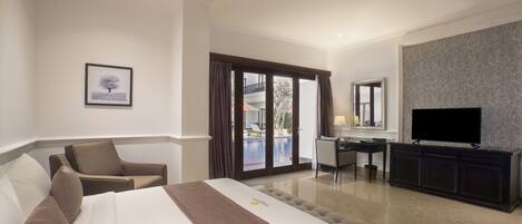 A hotel room with a bed, a desk, a chair, a TV, and a view of an outdoor swimming pool.