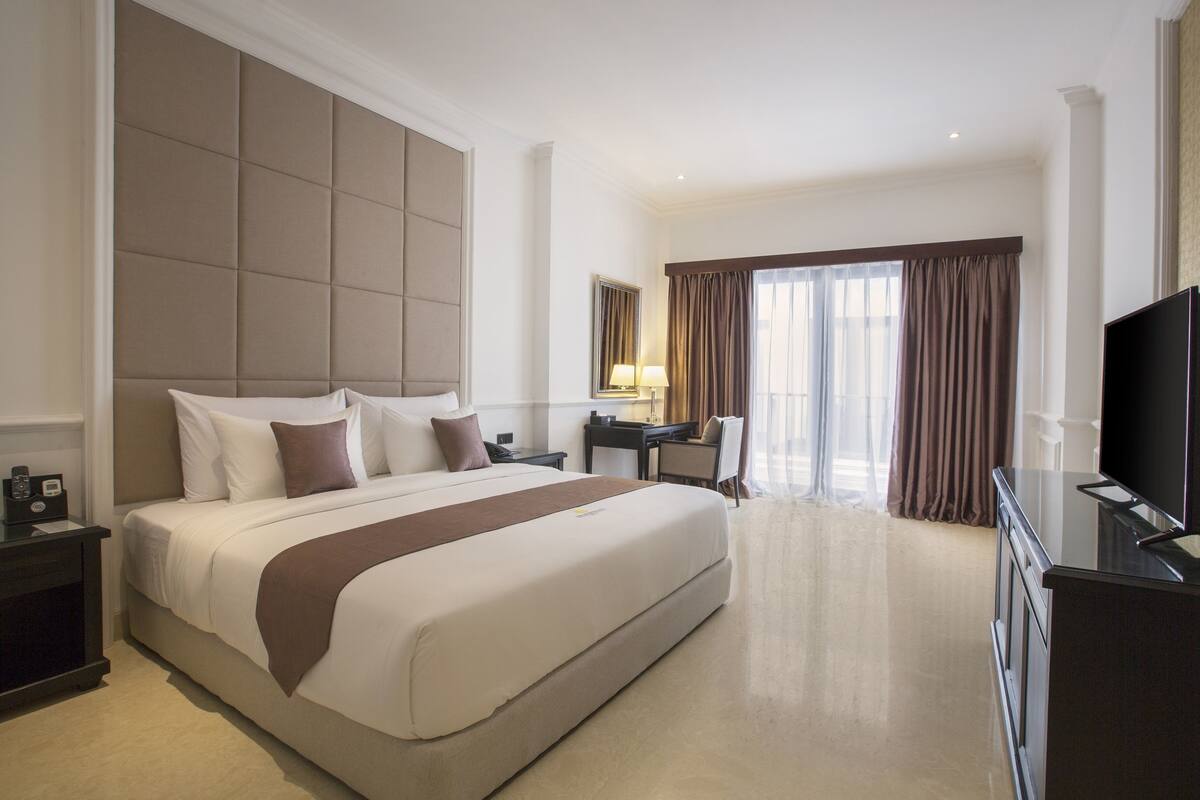 Une chambre d’hôtel spacieuse, dotée d’un grand lit, d’un bureau, d’une chaise, d’une télévision et d’une fenêtre avec des rideaux.