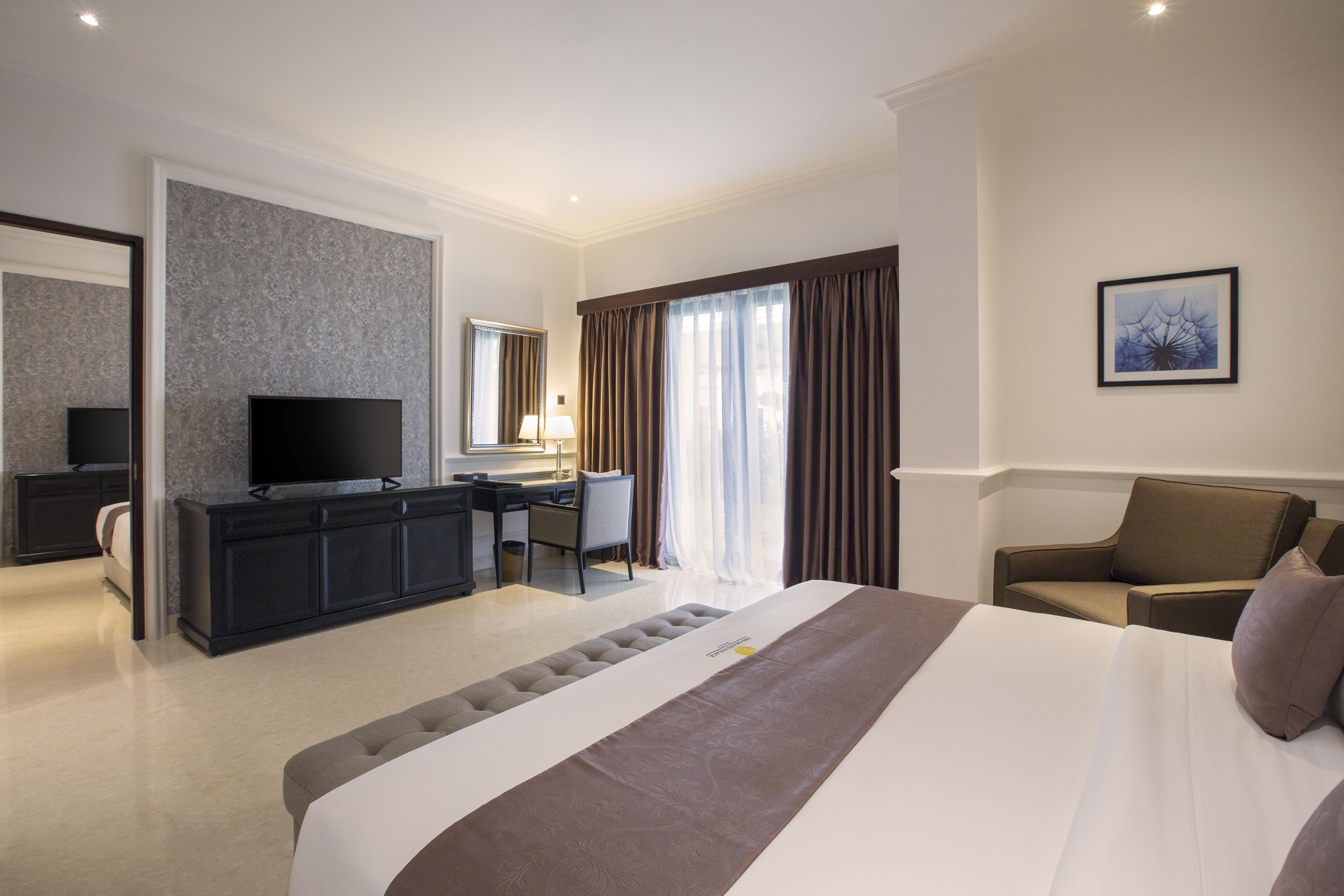 Quarto de hotel com uma cama grande, uma escrivaninha com cadeira, televisão e janela com cortinas.