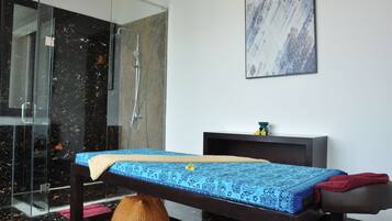 Relax in this serene spa room featuring a massage table, glass-enclosed shower, and soothing artwork.