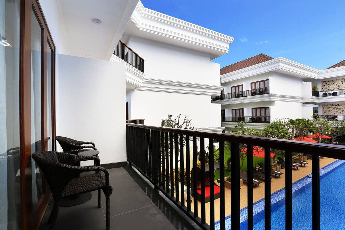 Un balcon avec des fauteuils en osier, une piscine et une vue sur un jardin aménagé.