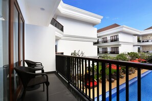 A balcony with wicker chairs, a pool, and a view of a landscaped garden. - Grand Palace Hotel Sanur - Bali (Denpasar)