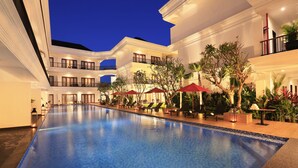 A hotel pool area with a long, rectangular pool, multiple lounge chairs, and umbrellas.