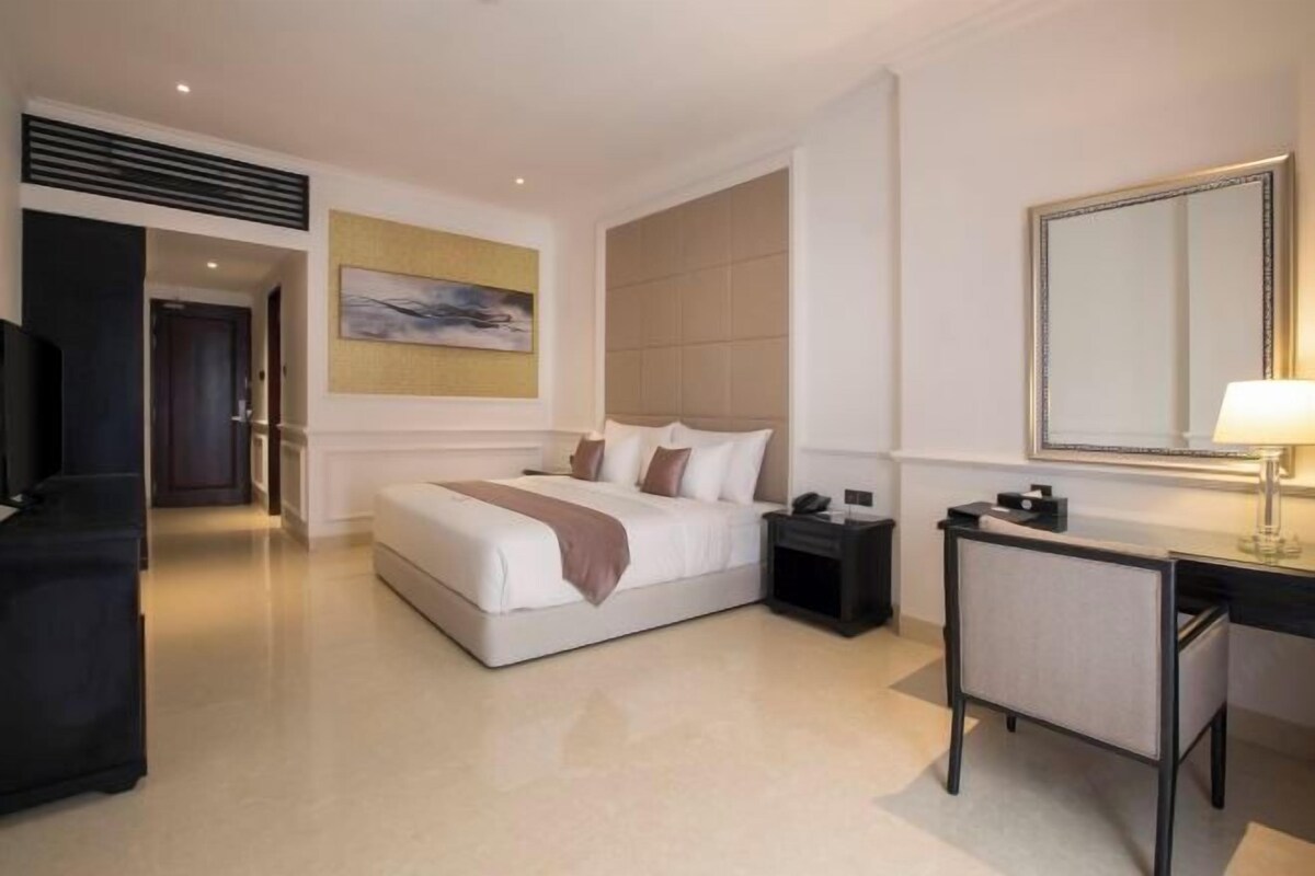 Een moderne hotelkamer met een groot bed, een bureau, een stoel, een nachtkastje, een spiegel en een schilderij aan de muur.