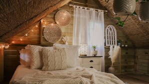 A cozy bedroom with a wooden ceiling, a bed with white bedding, a nightstand, and a window with curtains. - Hacienda Tres Casitas (Cabo Rojo)