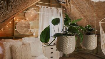 A cozy room with a wooden ceiling, a bed with white bedding, and hanging planters with green plants.