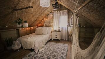 Un dormitorio acogedor en el ático, con techo inclinado, cama con ropa de cama blanca, alfombra estampada y lámpara colgante.