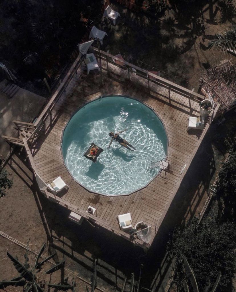A circular pool with a wooden deck, surrounded by lounge chairs and a small table.