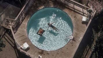A circular pool with a wooden deck, surrounded by lounge chairs and a small table.