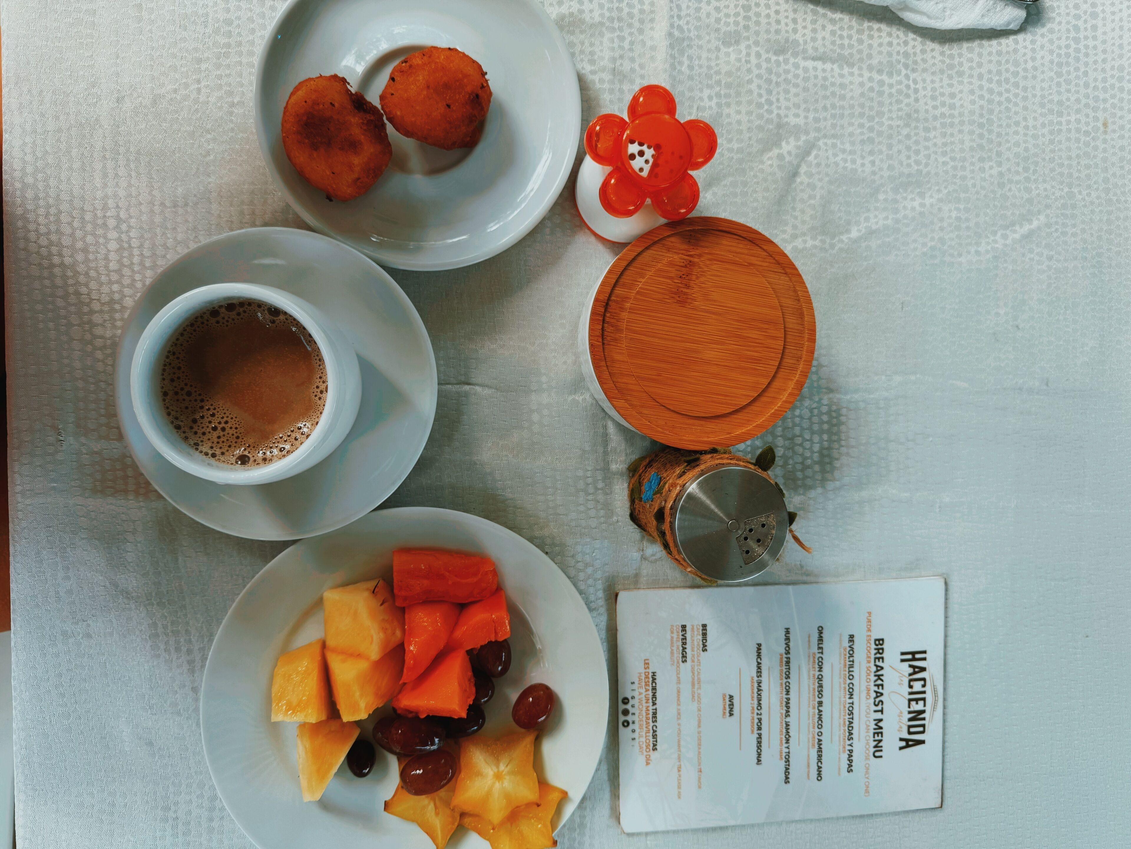 A breakfast setting with a menu, a cup of coffee, two fried items, and a plate of fruit.
