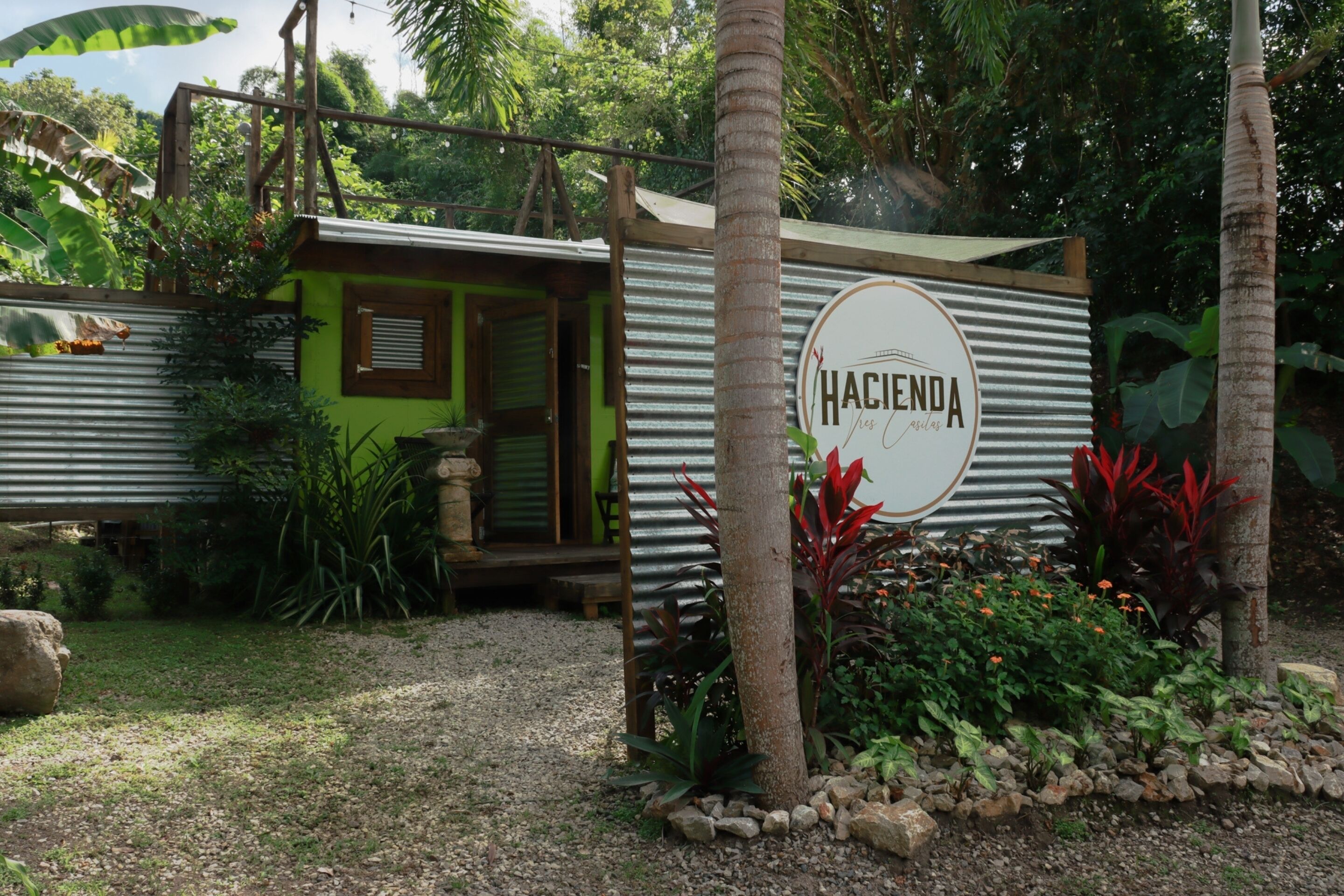 Uma cabana rústica com fachada verde, uma porta de madeira e uma placa com a inscrição 'Hacienda'.