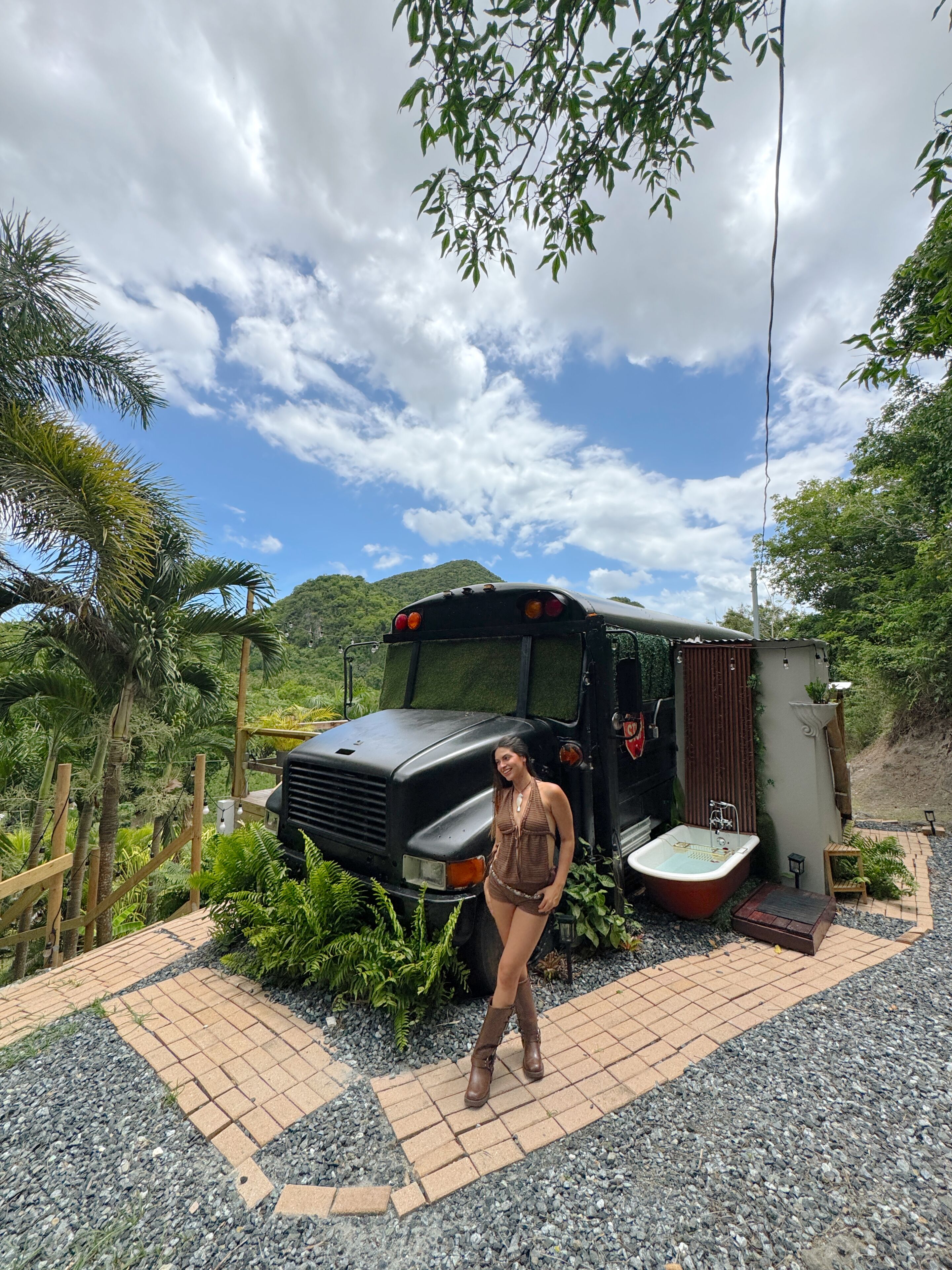 A bus parked in a natural setting with a small outdoor shower and a wooden deck.