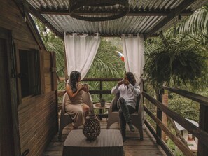 A wooden deck with two wicker chairs, a woven table, and a potted plant. - Hacienda Tres Casitas (Cabo Rojo)