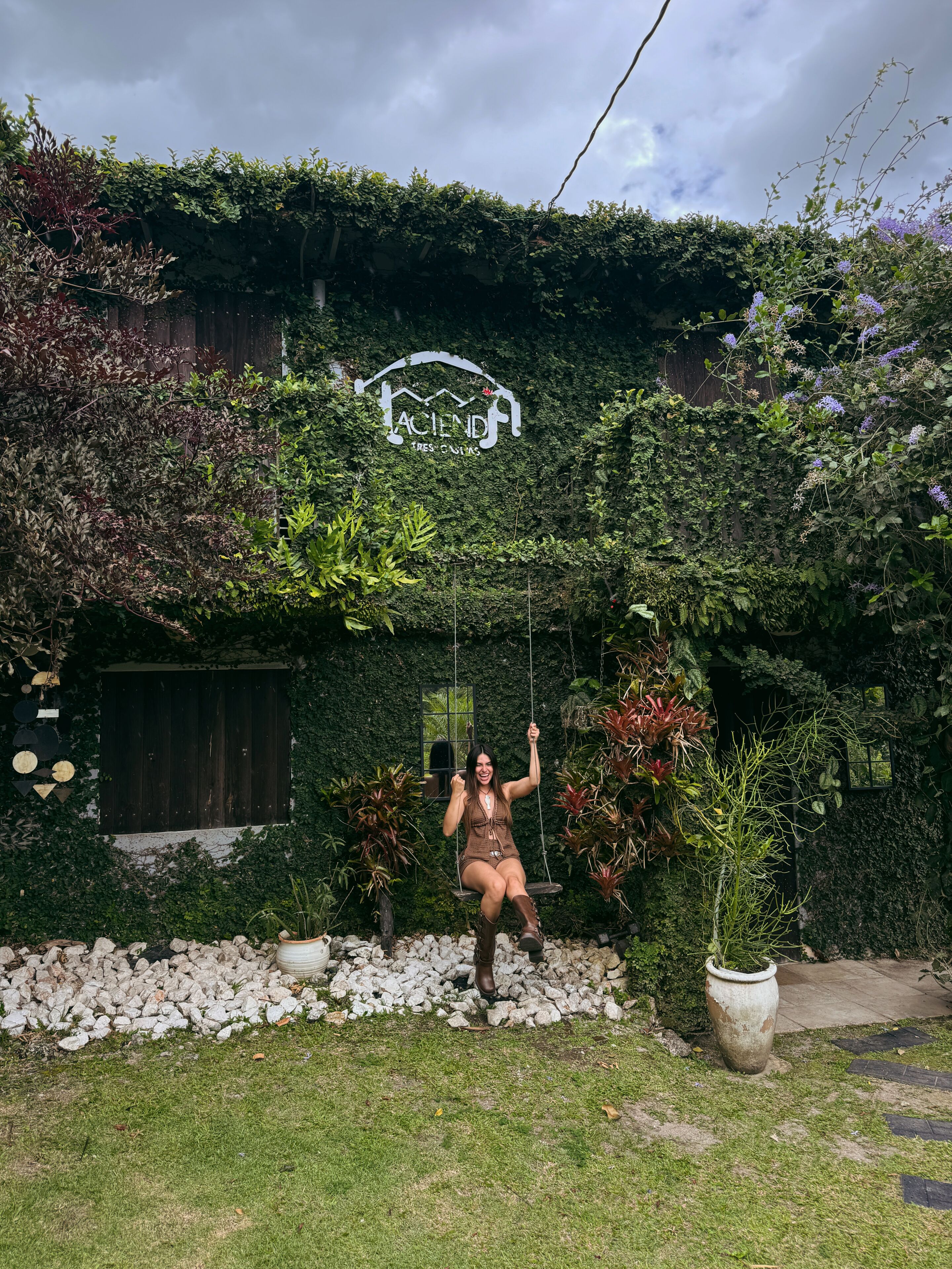 A person on a swing in a garden with a sign above.