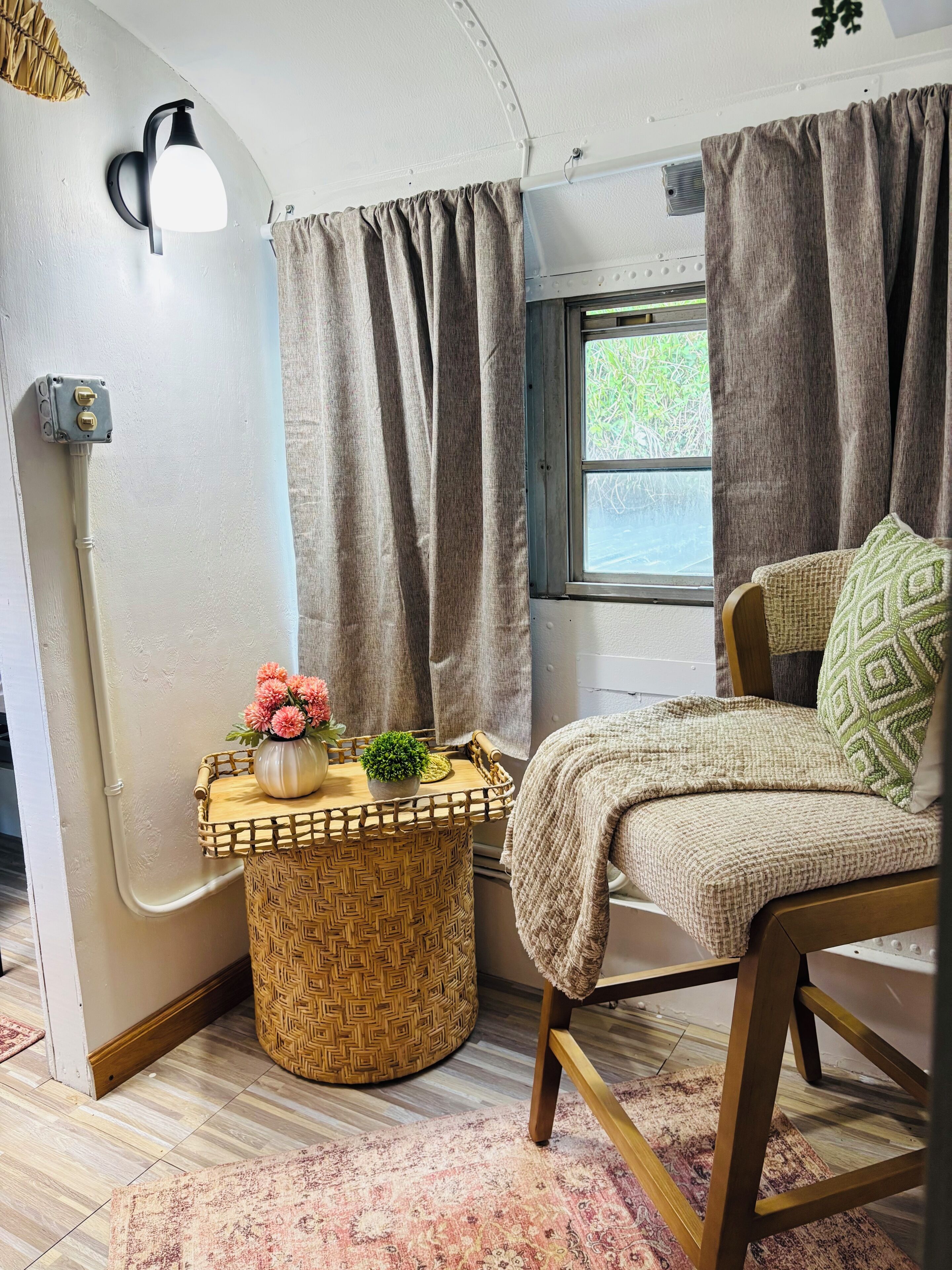 A cozy interior with a bed, a small table with flowers, a lamp, and a window with curtains.