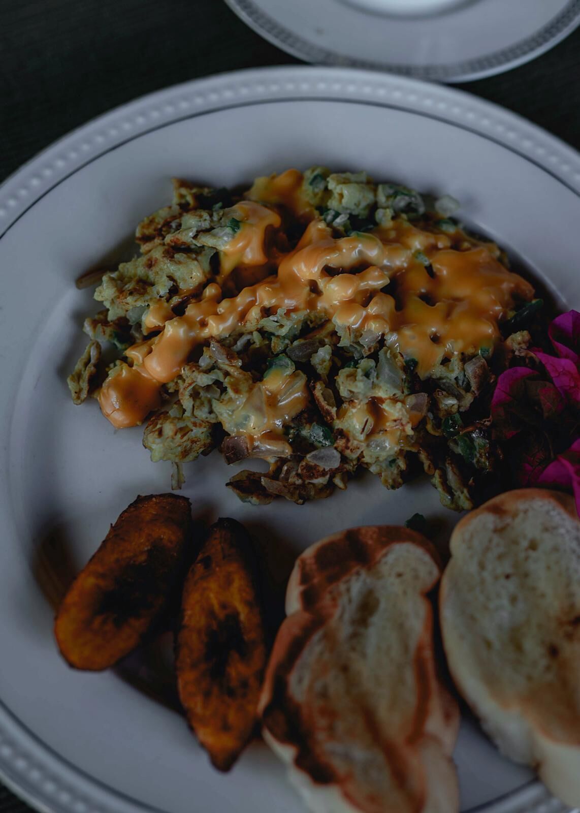 Un plat amb un plat principal cobert amb una salsa cremosa, acompanyat de patates rostides i trossos de pa.