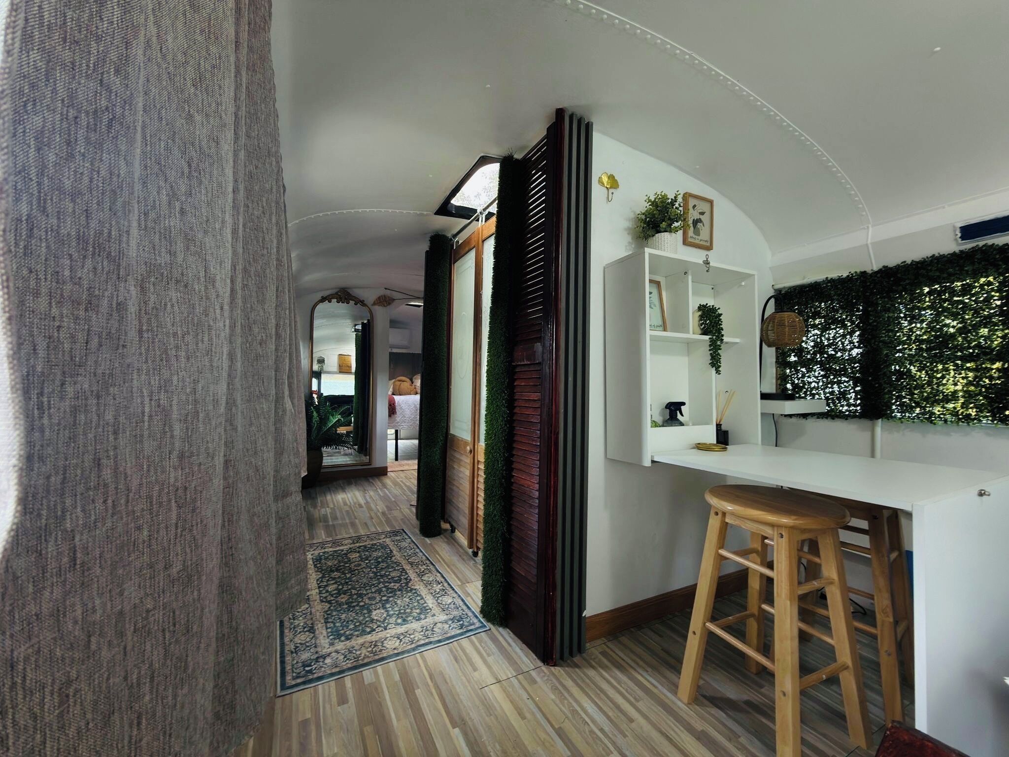 Um interior moderno com piso de madeira, uma parede branca com parede verde de plantas, um banquinho de madeira e um espelho.