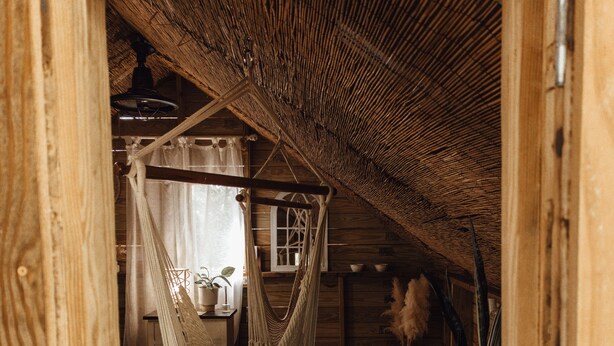 A cozy wooden cabin interior with a hammock, a small table, and a potted plant. - Hacienda Tres Casitas (Cabo Rojo)