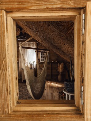 A cozy wooden cabin interior with a hammock, a small table, and a potted plant. - Hacienda Tres Casitas (Cabo Rojo)