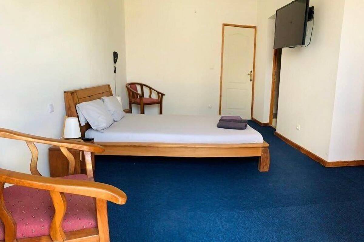 A single-bed room with a wooden headboard, a chair, a television mounted on the wall, and a door.