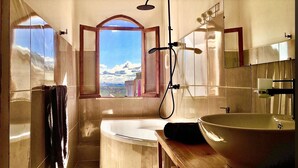 A bathroom with a bathtub, a large mirror, and a view of a snowy landscape through a window. - Iarimbato Hotel (Antananarivo)