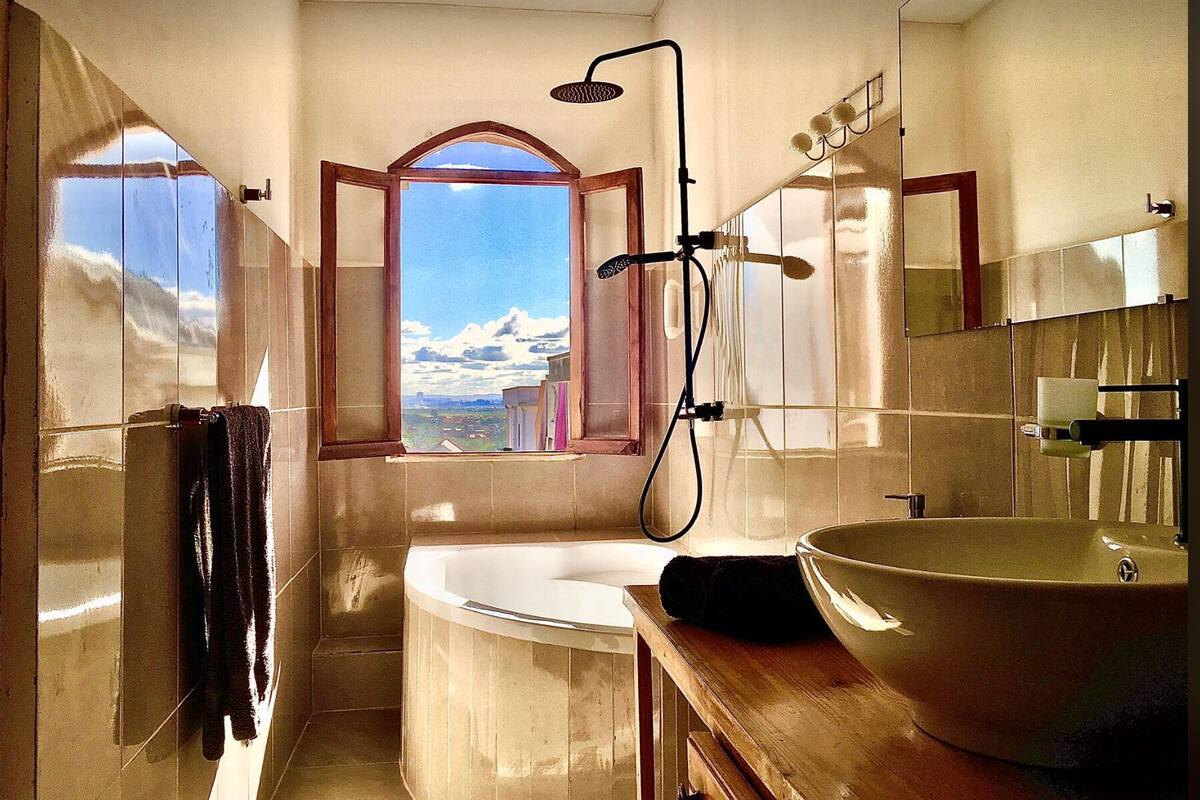 A bathroom with a bathtub, a large mirror, and a view of a snowy landscape through a window.