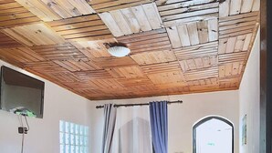 A room with a wooden ceiling, a bed, a desk, a chair, and a window with curtains. - Iarimbato Hotel (Antananarivo)