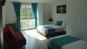 Habitación de hotel con dos camas, una silla roja, un televisor y un cuadro en la pared.