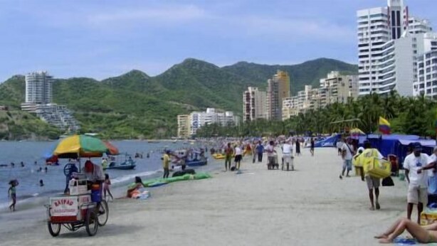Una playa con gente, un carrito de ventas y edificios al fondo.