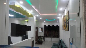Zona de recepción con un panel de vidrio, mostrador de recepción, área de descanso con sillas y una pared decorada con una obra enmarcada.