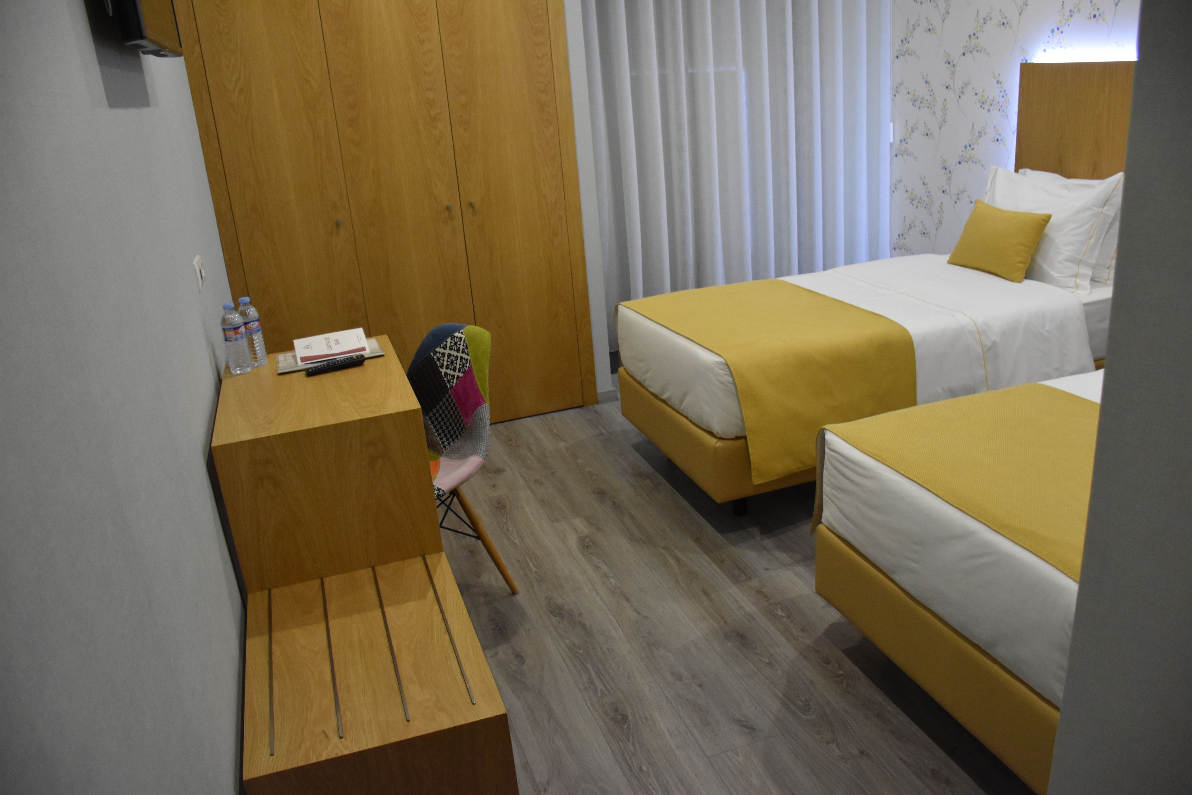Una habitación de hotel con dos camas, un escritorio de madera, una silla y una ventana con cortinas.