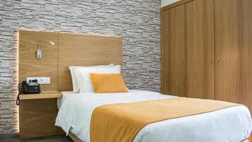 Una habitación de hotel moderna con pared de diseño de piedra, cabecera de madera, teléfono en la mesita de noche y armario.