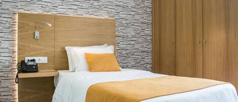 Una habitación de hotel moderna con pared de diseño de piedra, cabecera de madera, teléfono en la mesita de noche y armario.