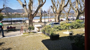 Un espacio pavimentado con bancos, plantas en macetas y vistas al río y embarcaciones.