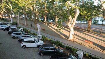 A parking area with several cars, a pathway lined with trees, and a body of water in the background.