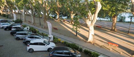 A parking area with several cars, a pathway lined with trees, and a body of water in the background.