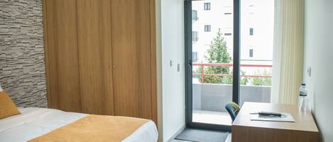 Habitación de hotel con cama, escritorio y vistas al balcón exterior.