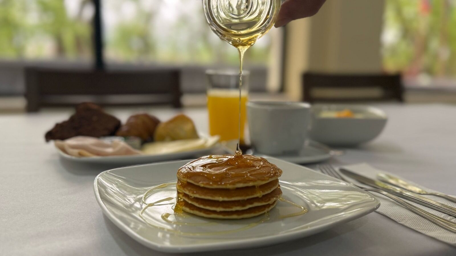 A stack of pancakes with syrup being poured on top, placed on a white plate.