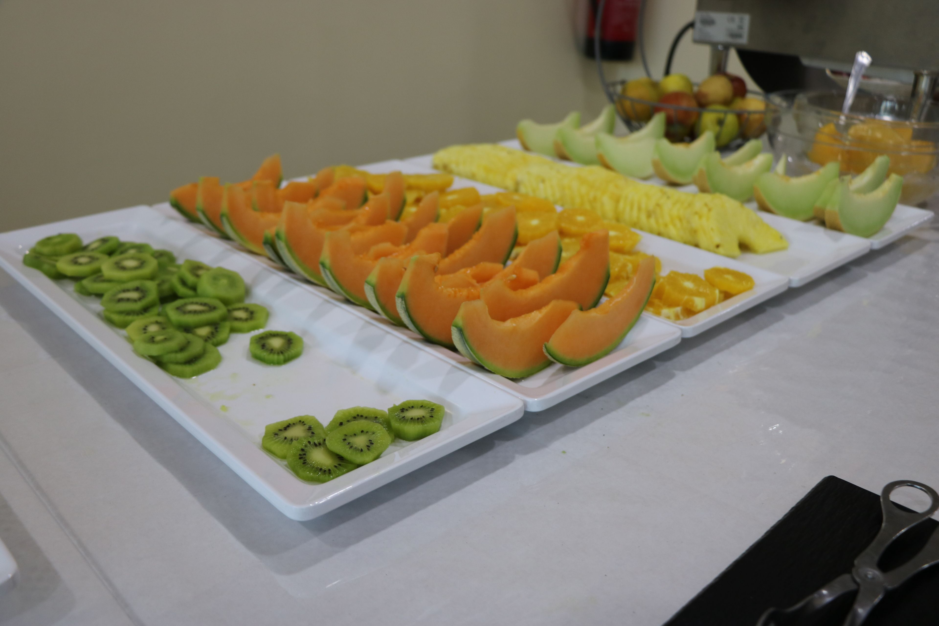 A buffet with sliced fruits including kiwi, cantaloupe, and pineapple.