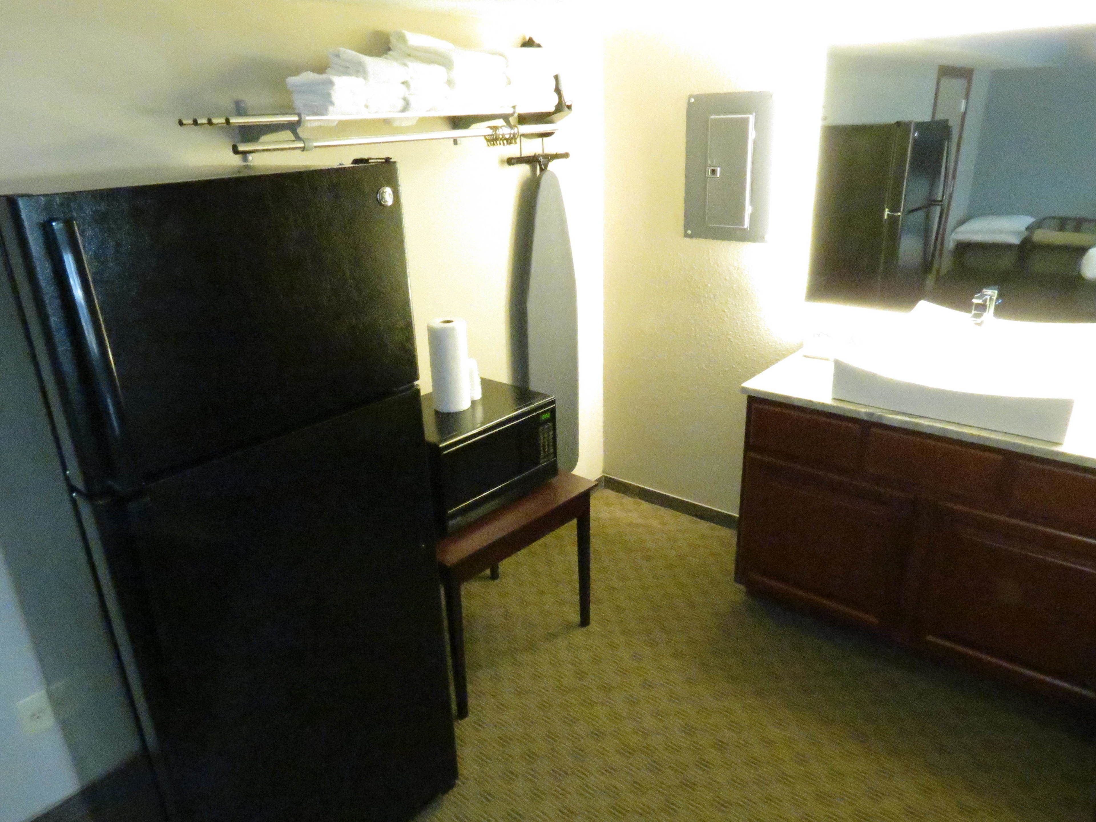 A compact hotel bathroom with a black refrigerator, a sink, and a mirror.