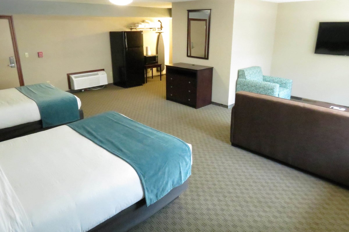 A hotel room with two beds, a desk, a chair, a dresser, and a television.