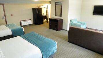 A hotel room with two beds, a desk, a chair, a dresser, and a television.