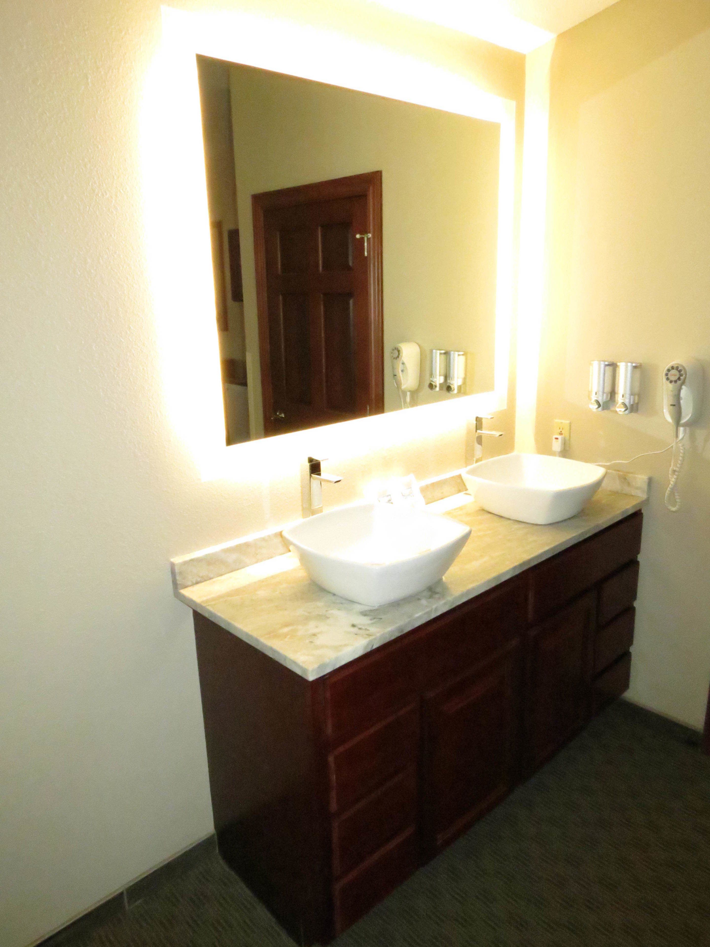 A bathroom with a large mirror, two sinks, and a marble countertop.