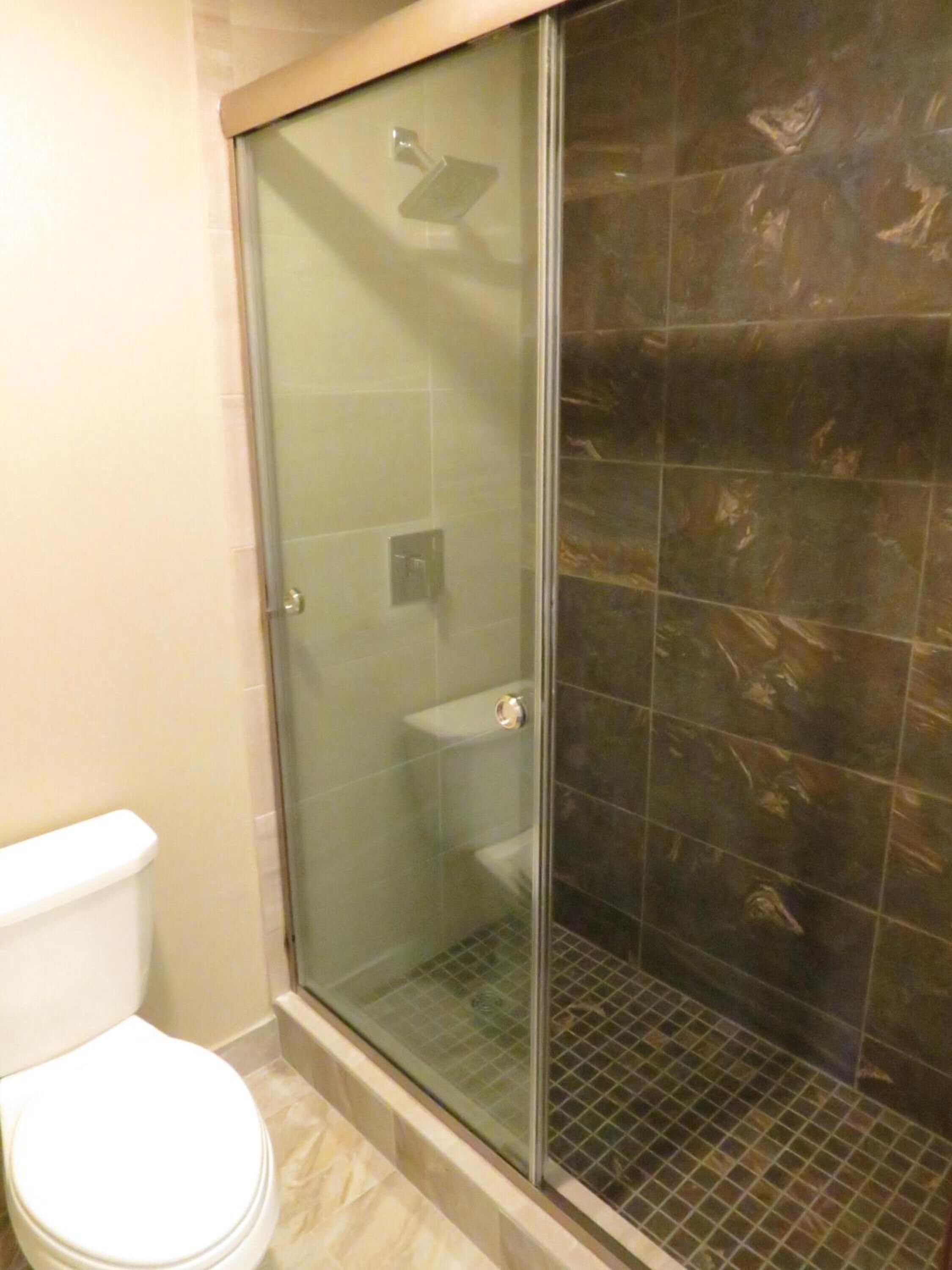 Une salle de bain avec une douche à parois de verre, des toilettes et des murs carrelés.