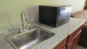 A kitchen with a stainless steel sink, a microwave, and wooden cabinets. - Edgewater Hotel (Put-in-Bay)