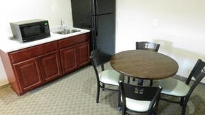 A compact kitchen with a microwave, sink, refrigerator, and a dining area with a round table and four chairs. - Edgewater Hotel (Put-in-Bay)