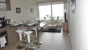 A modern kitchen with a dining area, white furniture, and a view of the beach. - Departamento Marina Horizonte 1 (Coquimbo)