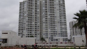 A high-rise residential building with multiple balconies, a modern architectural design, and a landscaped area with plants and a palm tree. - Departamento Marina Horizonte 1 (Coquimbo)